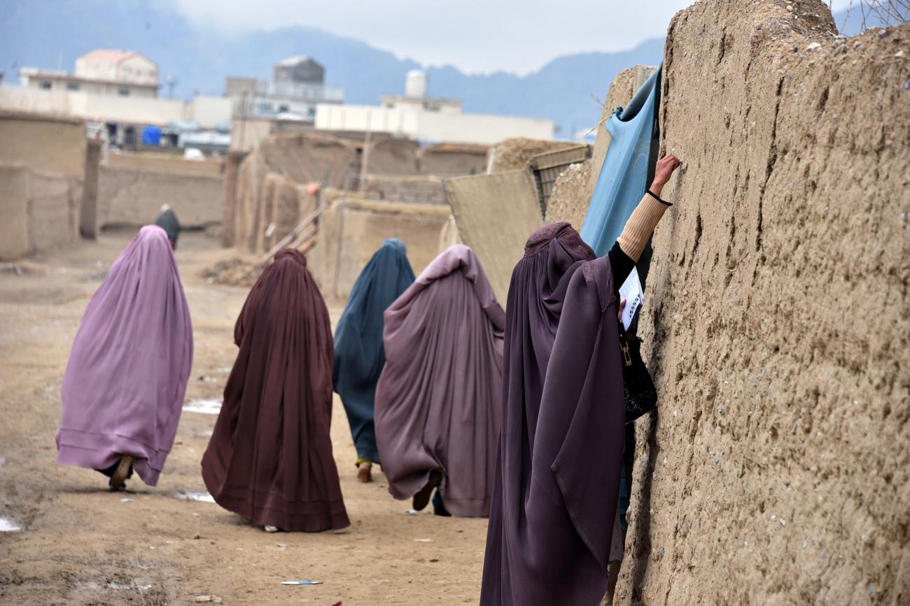 Women in lavender, blue, and burgundy burkas who are part of an immunization team write a message on the wall of a stone house during a vaccination campaign in Kandahar, Afghanistan on January 28, 2020. 