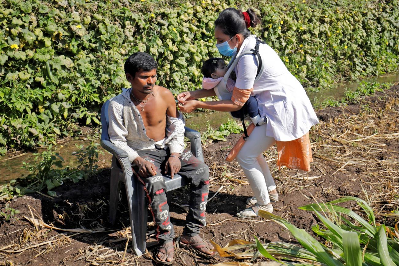 Asmita Koladiya, a health-care worker, carrying her eight-month-old daughter, gives a dose of vaccine against COVID-19 to a man in Lodhida village, in Gujarat, India, on February 2, 2022.