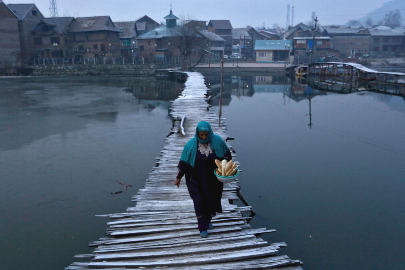 A woman dressed in a head covering and long dress carries bread as she walks on a frost-covered footbridge in the interiors of Nigeen Lake on a cold winter morning in Srinagar, India, December 24, 2020. REUTERS/Danish Ismail