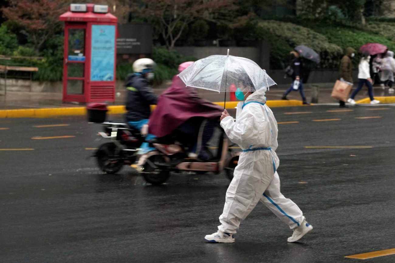 a worker in white protective suit holding an umbrella crosses a road in the rain during a COVID-19 outbreak in Shanghai, China, on November 30, 2022.