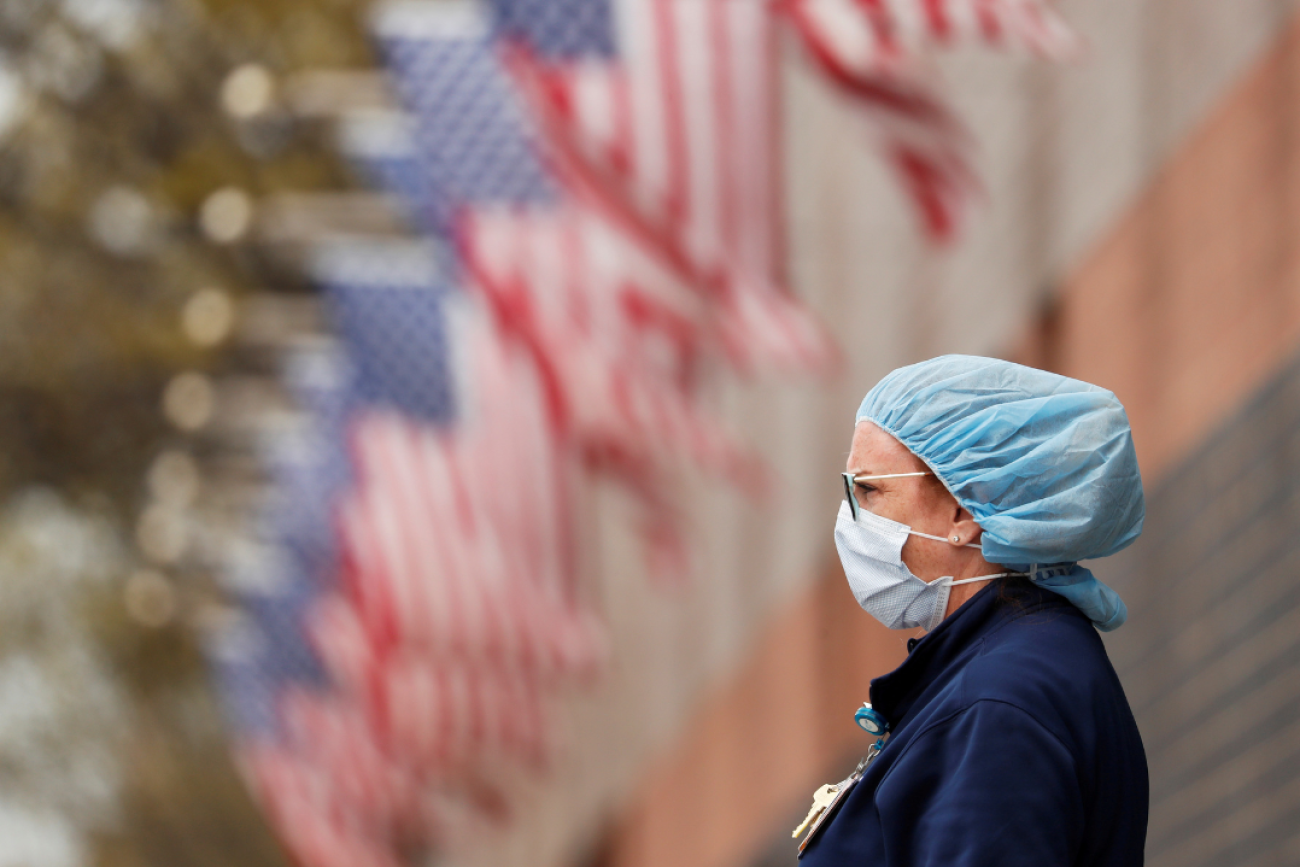 A nurse, seen in profile with a long row of American flags behind her, watches an ambulance driving away outside of Elmhurst Hospital during the COVID-19 pandemic, in Queens, New York, on April 20, 2020. 
