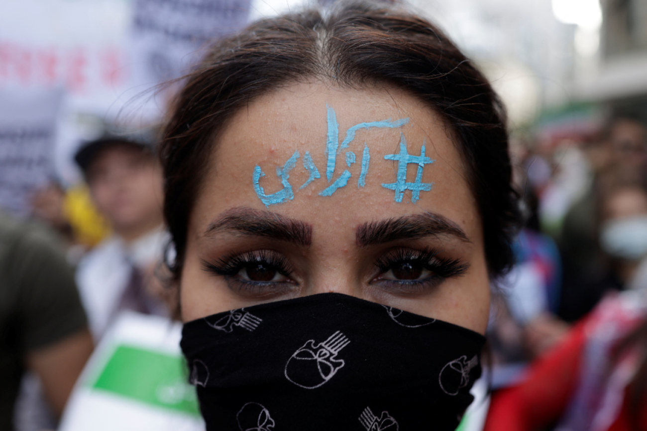 A woman wears a face mask and has the words "Freedom" written in blue paint on her forehead in Arabic. She takes part in a protest following the death of Mahsa Amini, near the Iranian consulate in Istanbul, Turkey, October 4, 2022. 