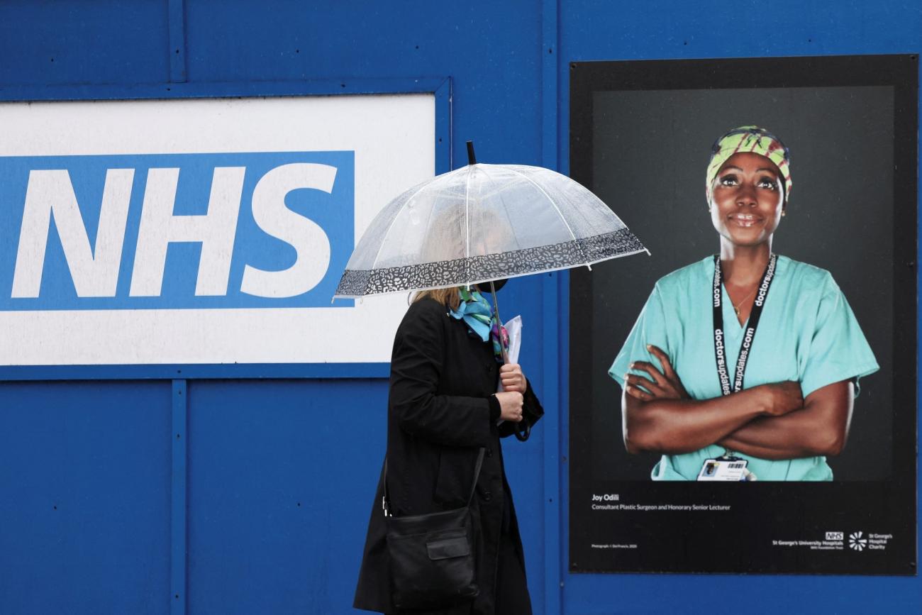 a woman walks past a poster of a NHS worker