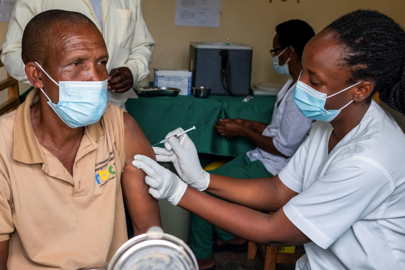 a man wearing a blue surgical mask receives a covid vaccination from a female nurse
