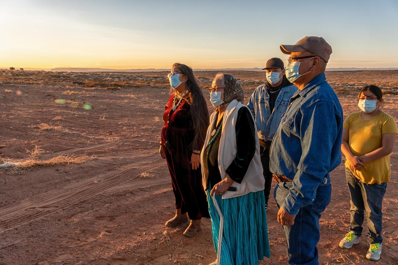 A Native American family is seen looking out at the sunset wearing masks.