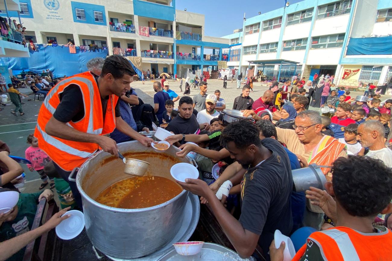 Palestinians, who fled their houses due to Israeli strikes, gather to get their share of charity food