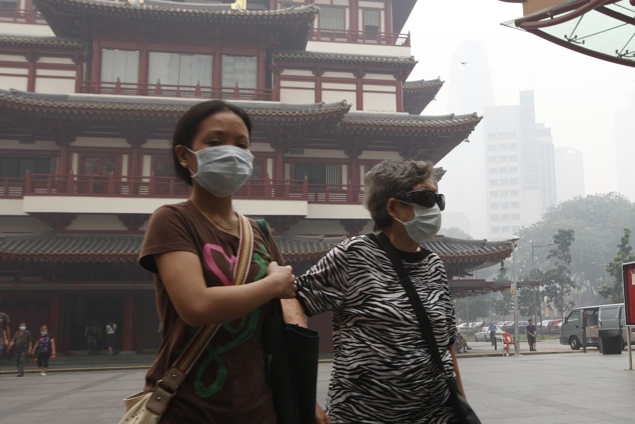 An elderly woman in face mask is accompanied by a helper as she walks in Singapore's Chinatown