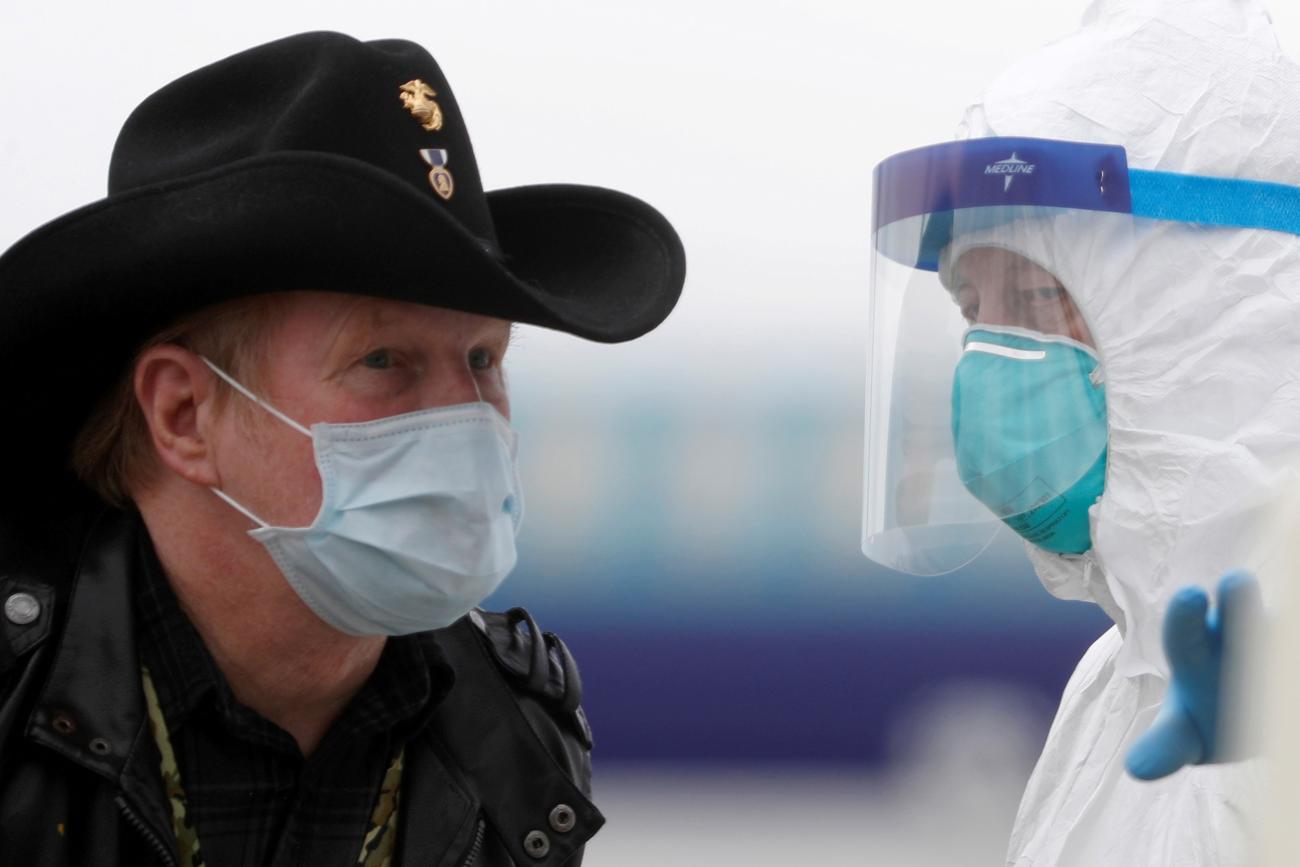 A worker in protective gear directs a masked passenger disembarking from the cruise ship Grand Princess in Oakland, California on March 10, 2020 amid concern over the growing COVID-19 pandemic. The picture shows a man wearing a mask and a cowboy hat standing facing a health worker in full protective gear. REUTERS/Stephen Lam 