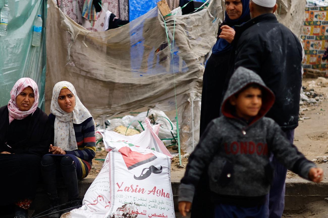 Palestinian women sit near bags of flour distributed by the United Nations Relief and Works Agency (UNRWA),