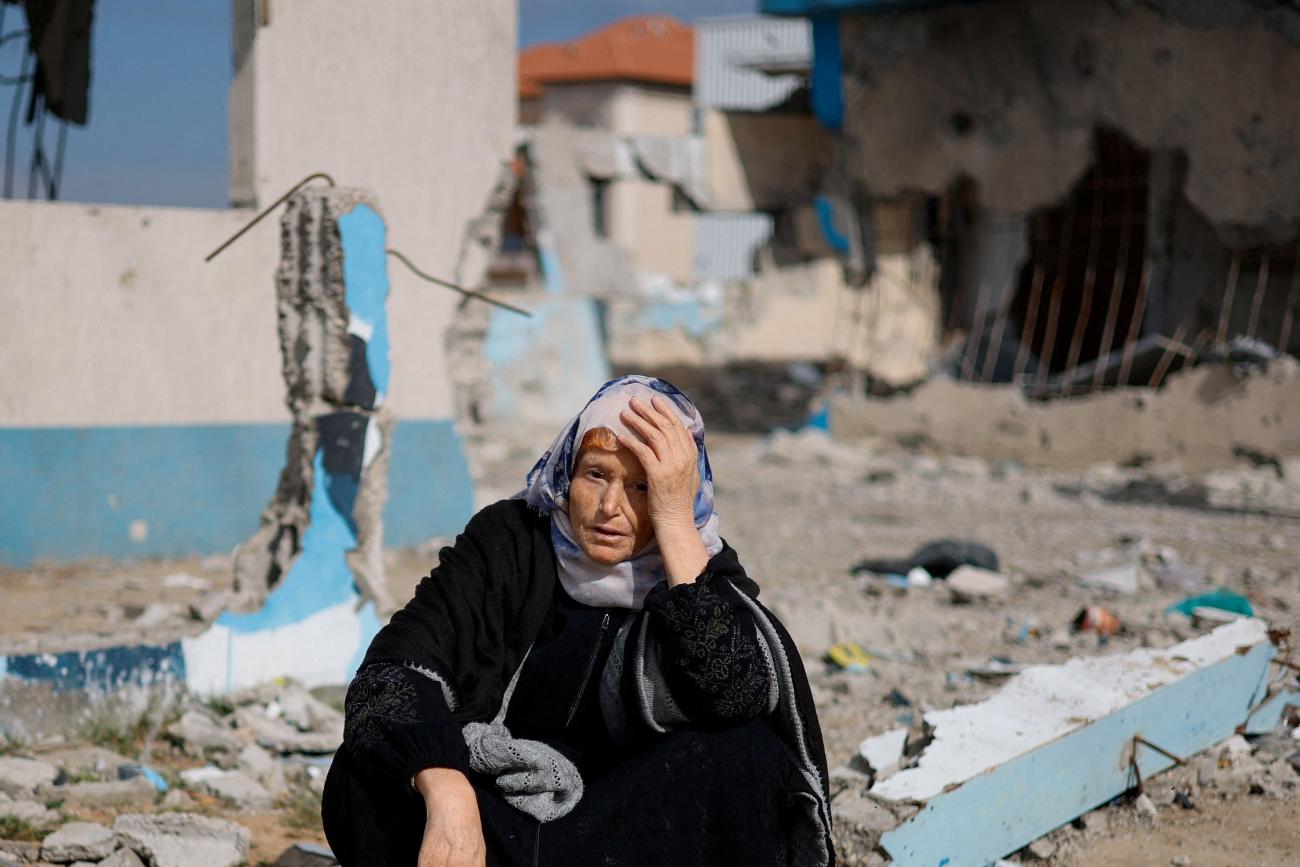 A woman rests next to a damaged building, as Palestinian arrive in Rafah after they were evacuated from Nasser hospital in Khan Younis.