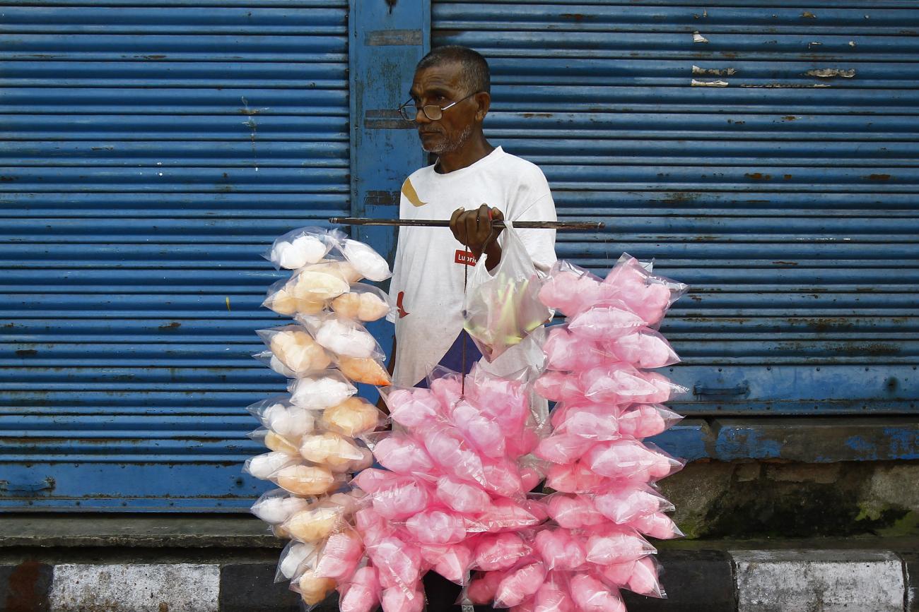 A vendor selling candy floss stands in front of closed shops along the roadside.