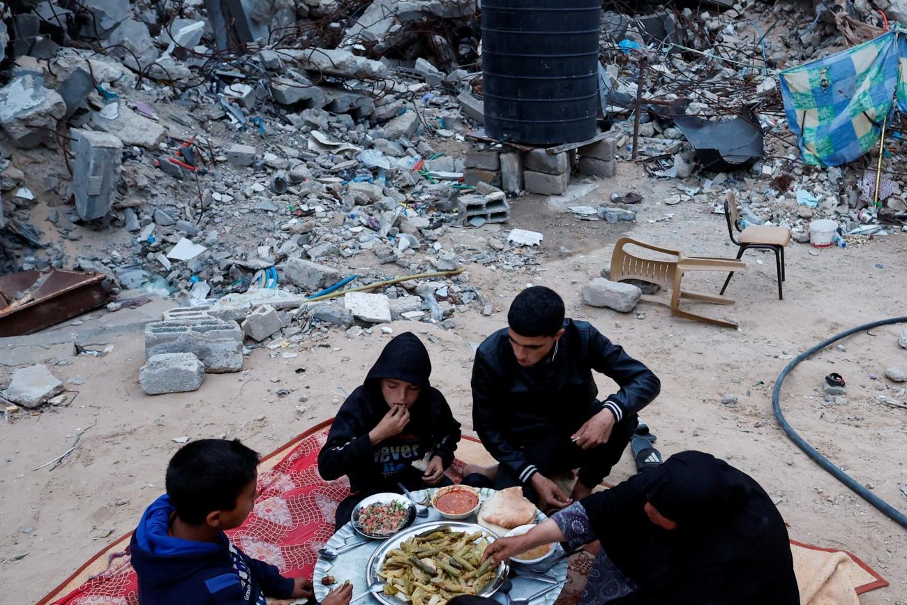 A Palestinian family eats their iftar meal they break their fast near the rubble of their destroyed house.