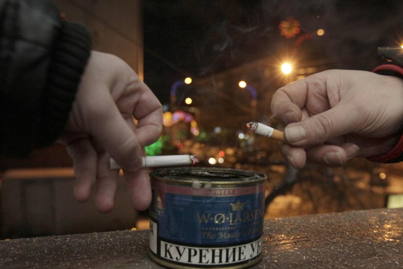 Men tap ash from their cigarettes while smoking on the balcony of an office building.