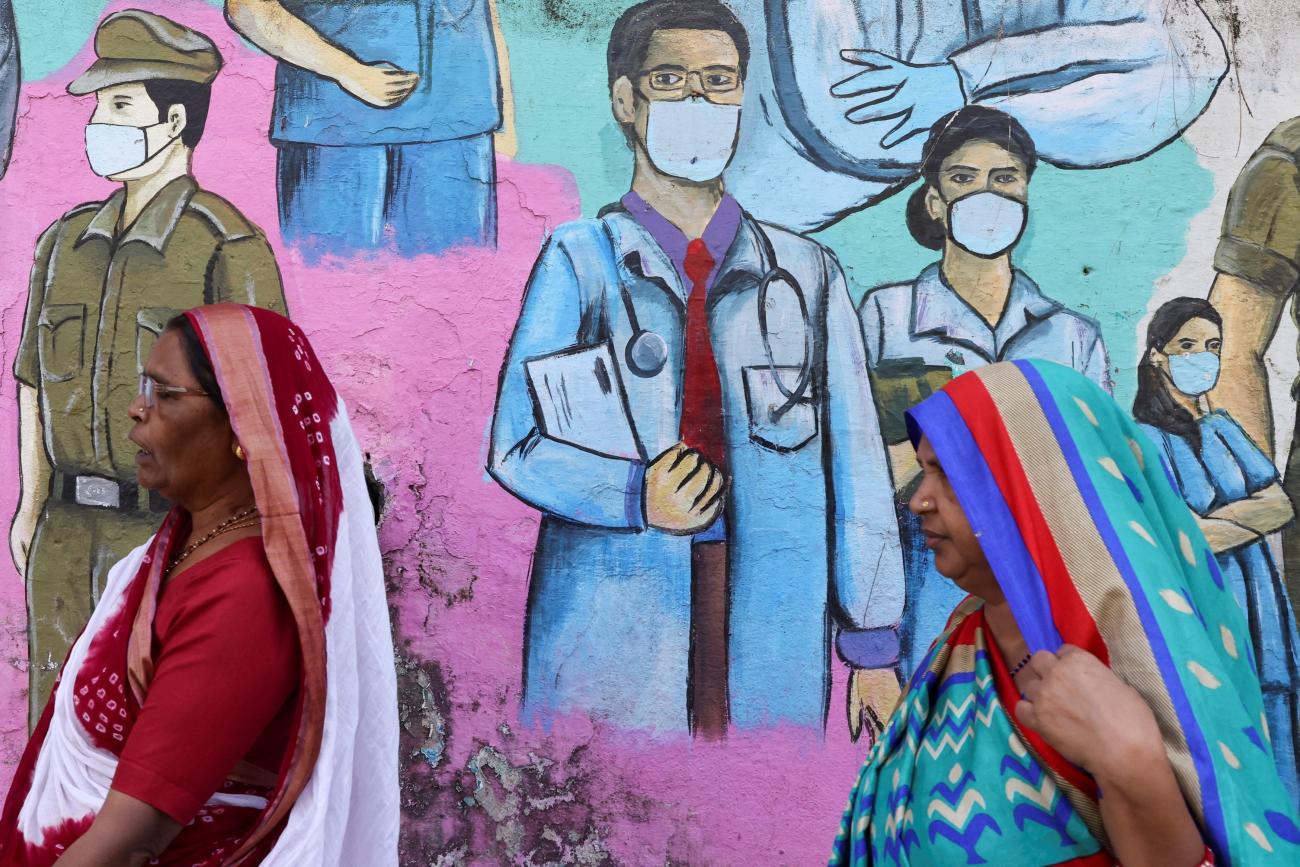 Women walk past a COVID-19 themed mural on the street.