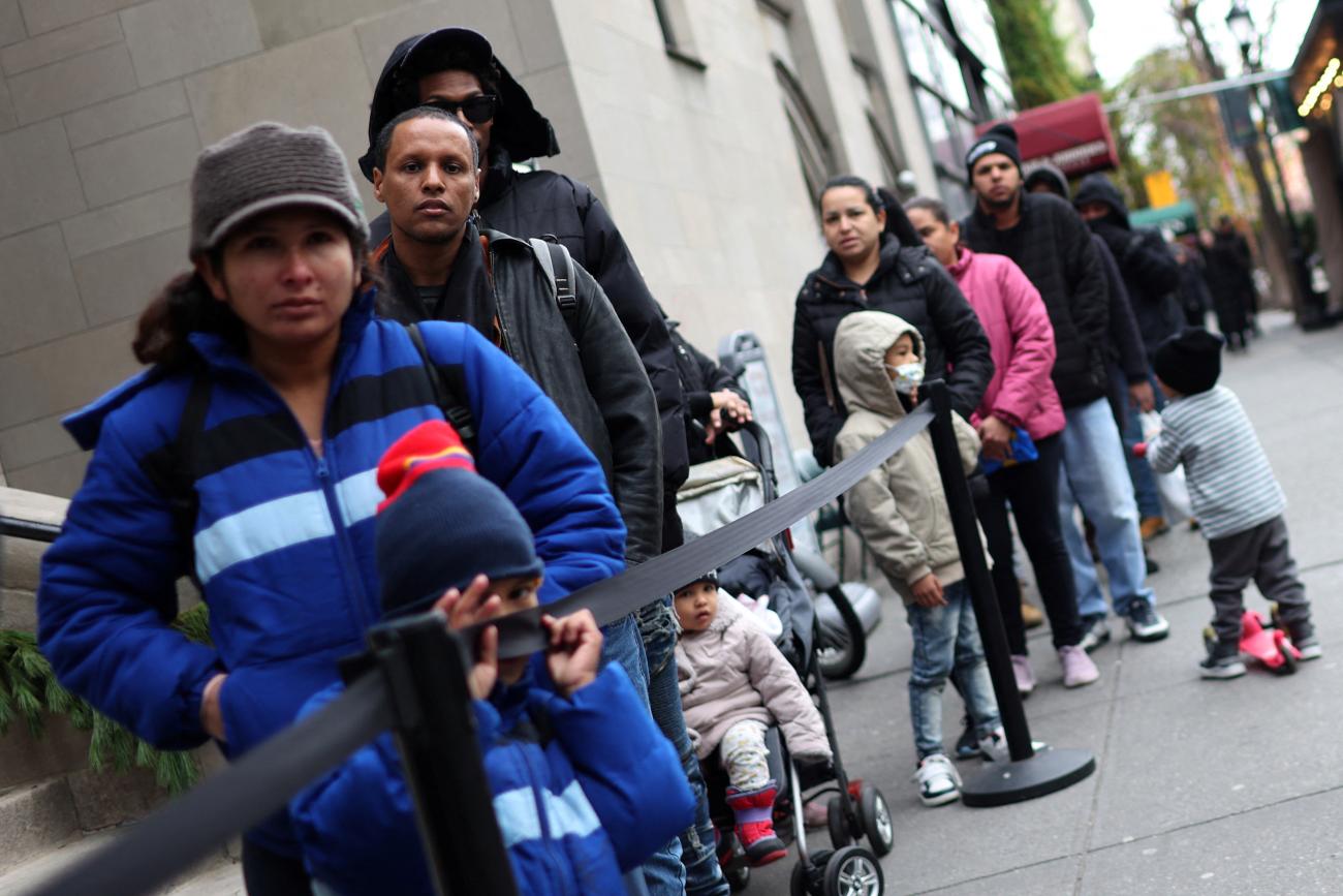 Recently arrived migrant families and others stand in line for a free meal provided by a Lutheran Church.