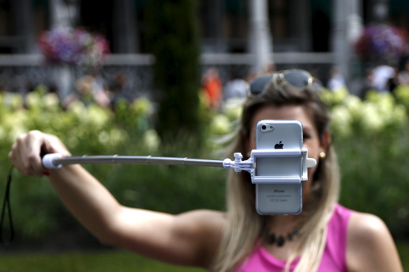 A tourist uses a selfie stick to take a photograph near a floral display.