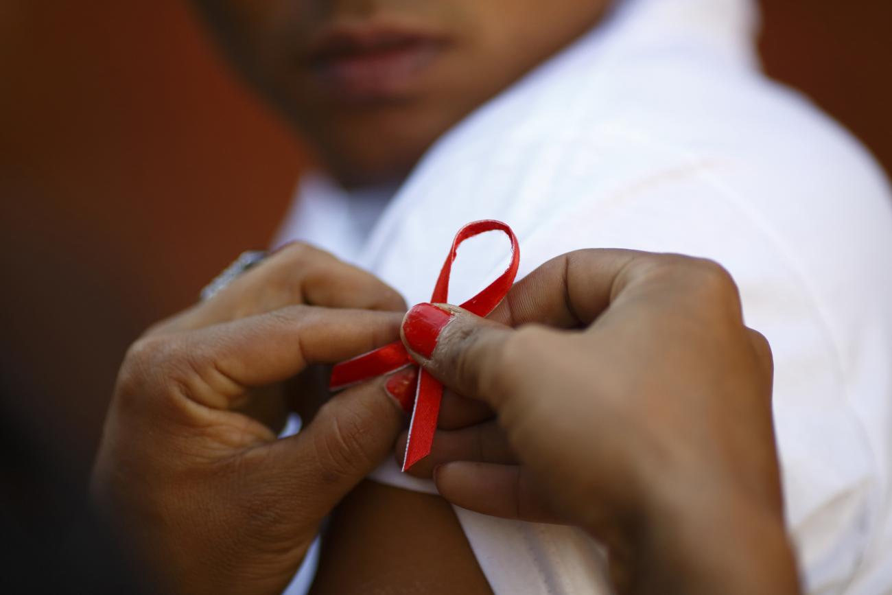 A red ribbon is put on the sleeves of a man by his friend to show support for people living with HIV, in Kathmandu, Nepal, on December 1, 2013.