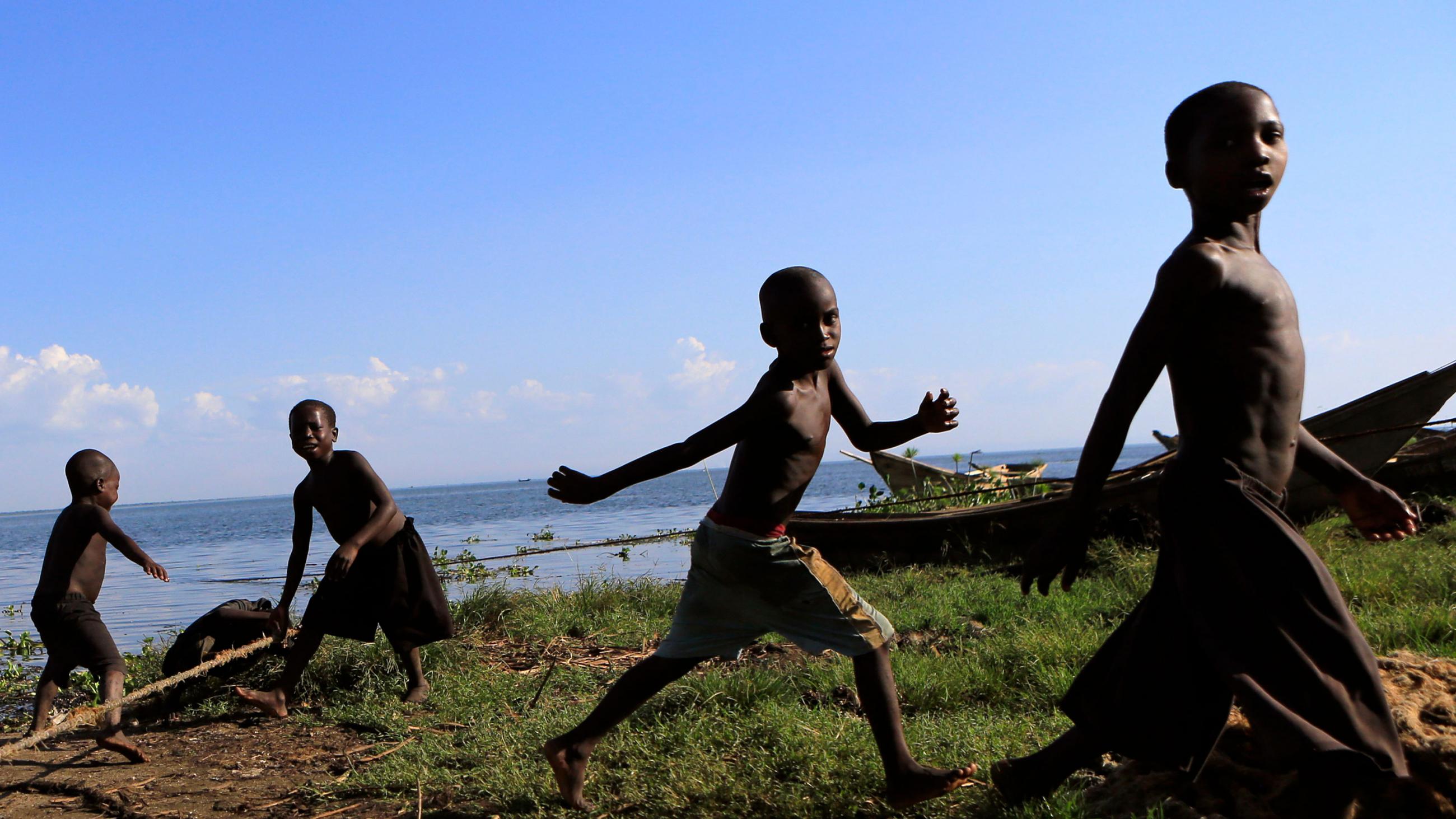 Children play along the shores of Lake Albert in Panyimur fishing village, north of Uganda's capital Kampala on November 30, 2013. Photo shows four boys in the approximate 5- to 10-year old age range running around a number of small fishing boats pulled up on shore.  