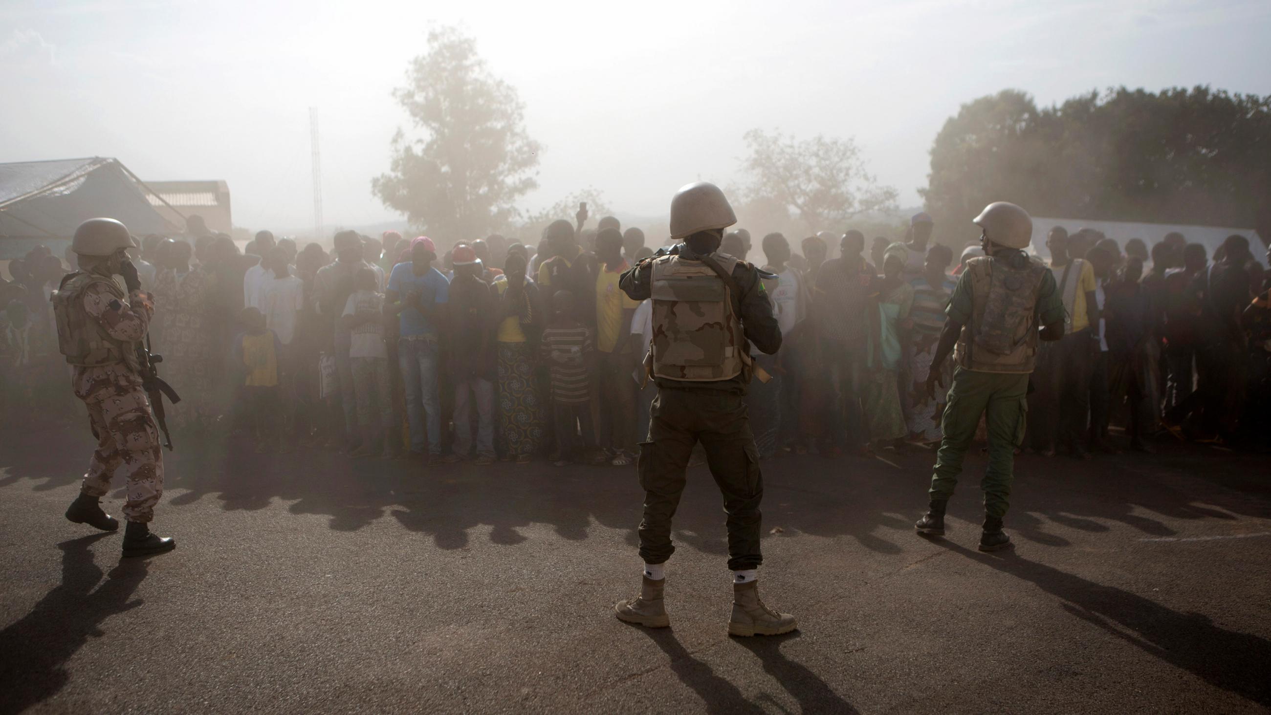 he picture shows a large crowd shrouded in what appears to be early morning mist with a thin line of heavily armed soldiers wearing combat fatigues standing between them and the camera. 