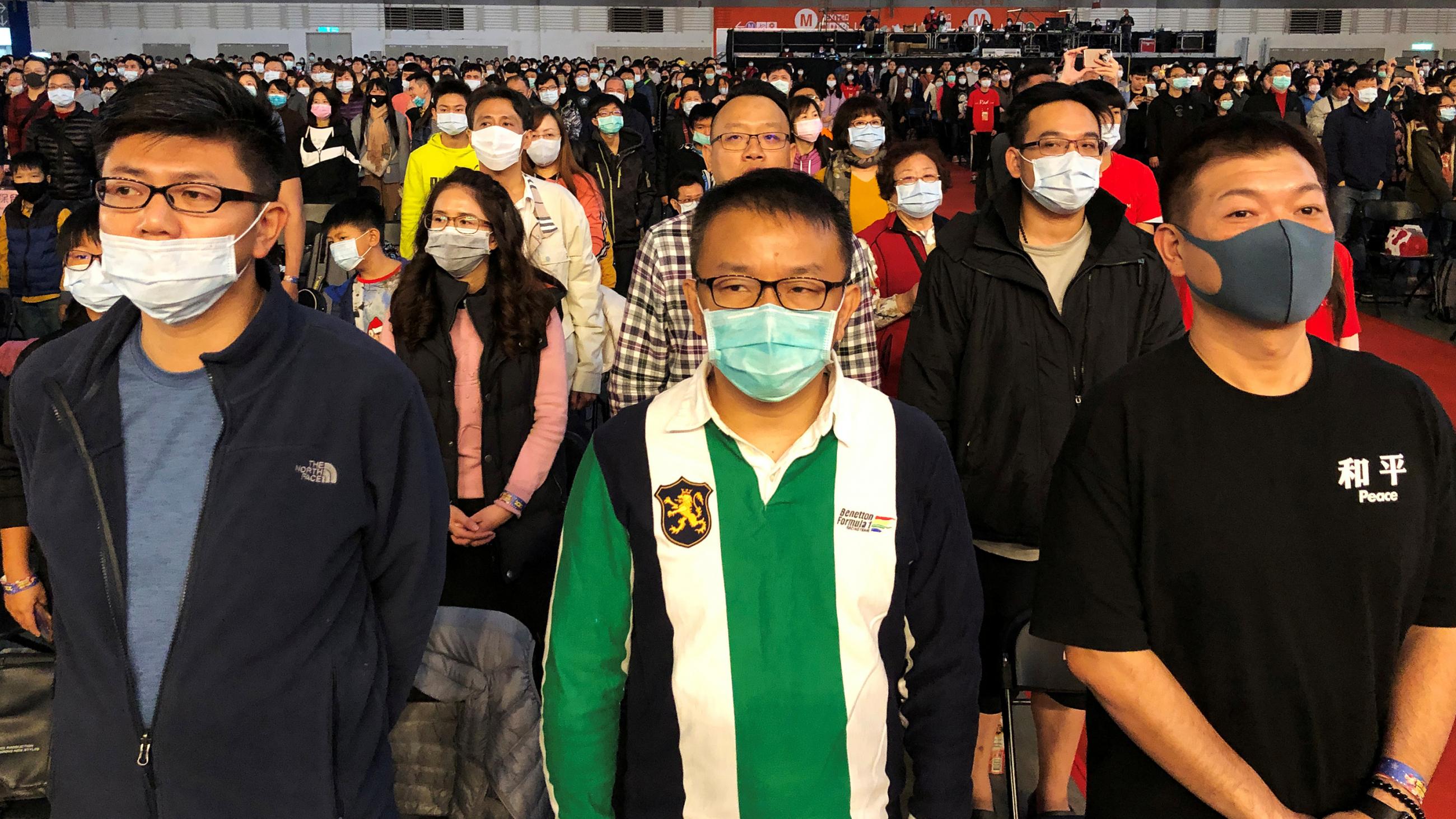 The photo shows a massive arena-like space filled with people, almost all of whom are wearing face masks.