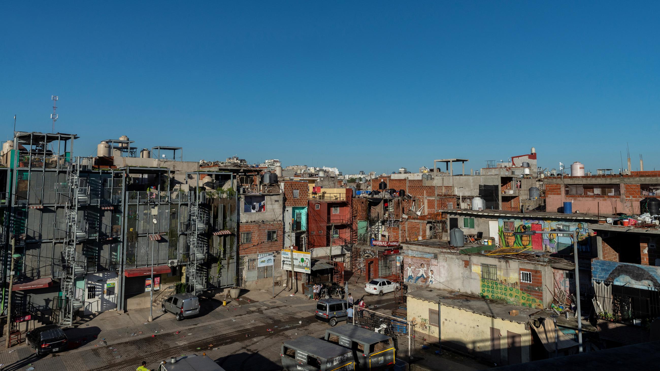 Photo shows a densely-packed brick and concrete community with box-like structures against a brilliant blue sky. 