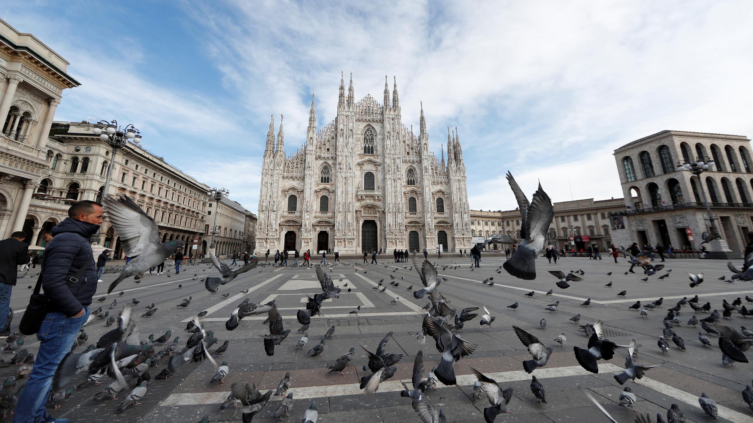 The photo is spectacular showing a full view of the iconic architectural landmark from across an almost empty square. In the foreground is a massive flock of birds captured in full flight. 