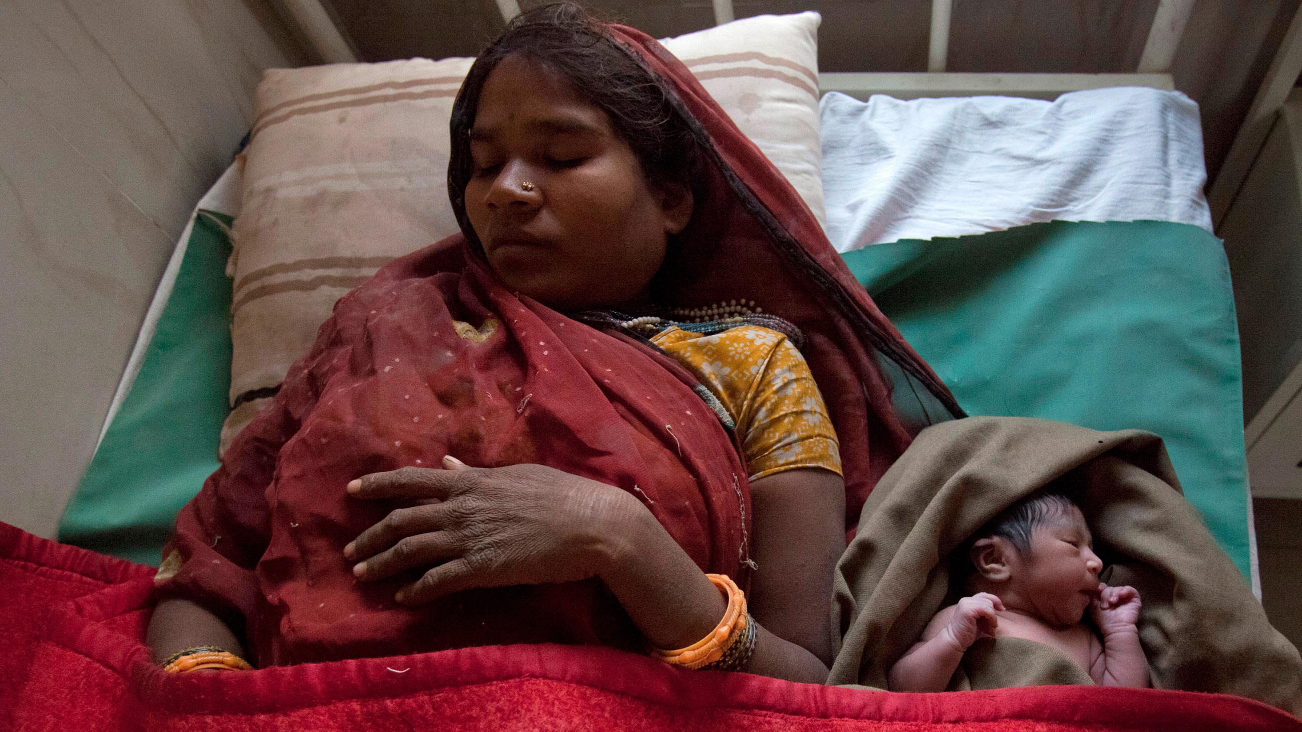 The photo shows mother and child both resting on a bed with a red blanket and a green sheet. 