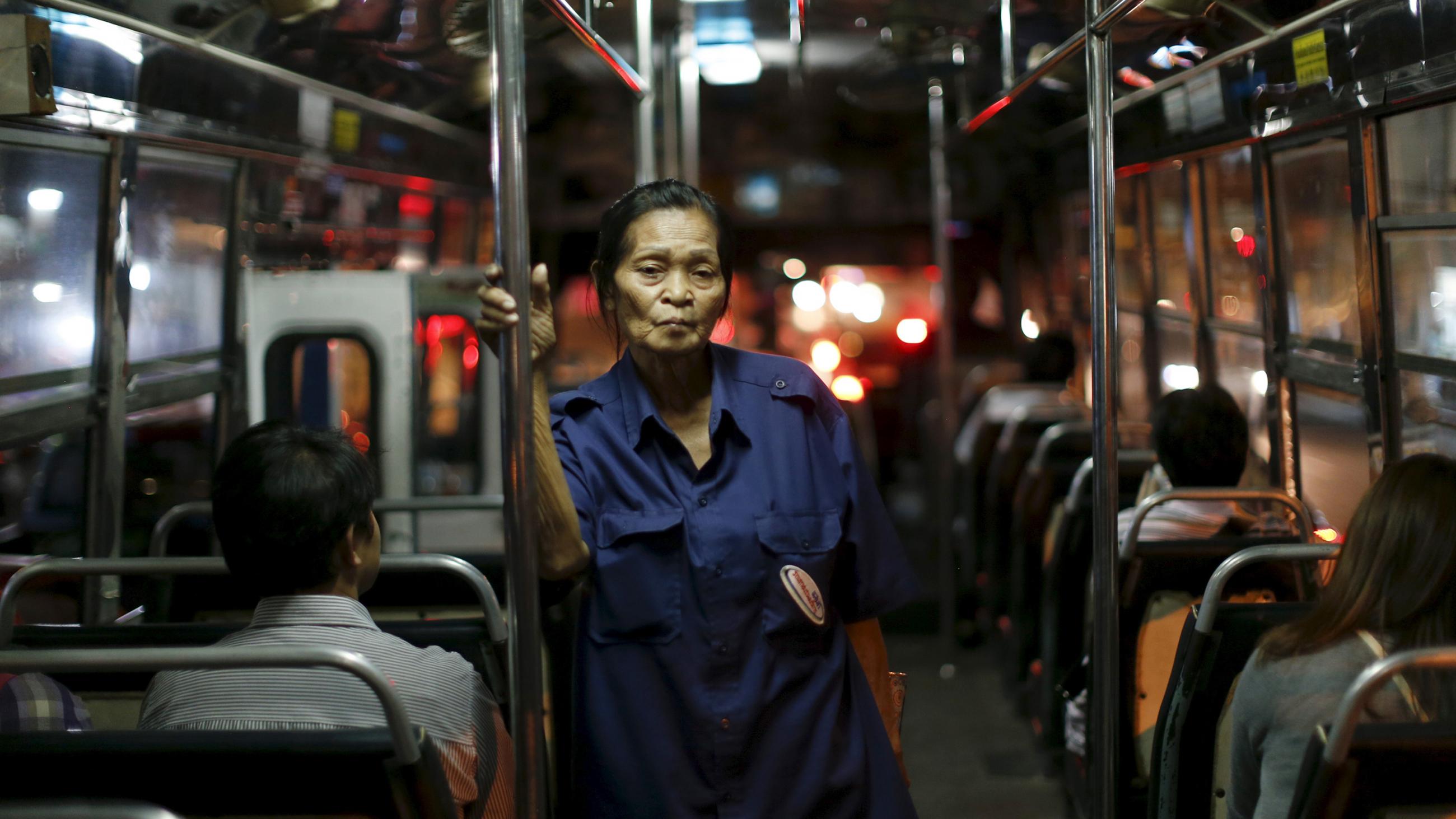 Picture shows the ticket taker standing on a bus at night, holding onto a rail. 