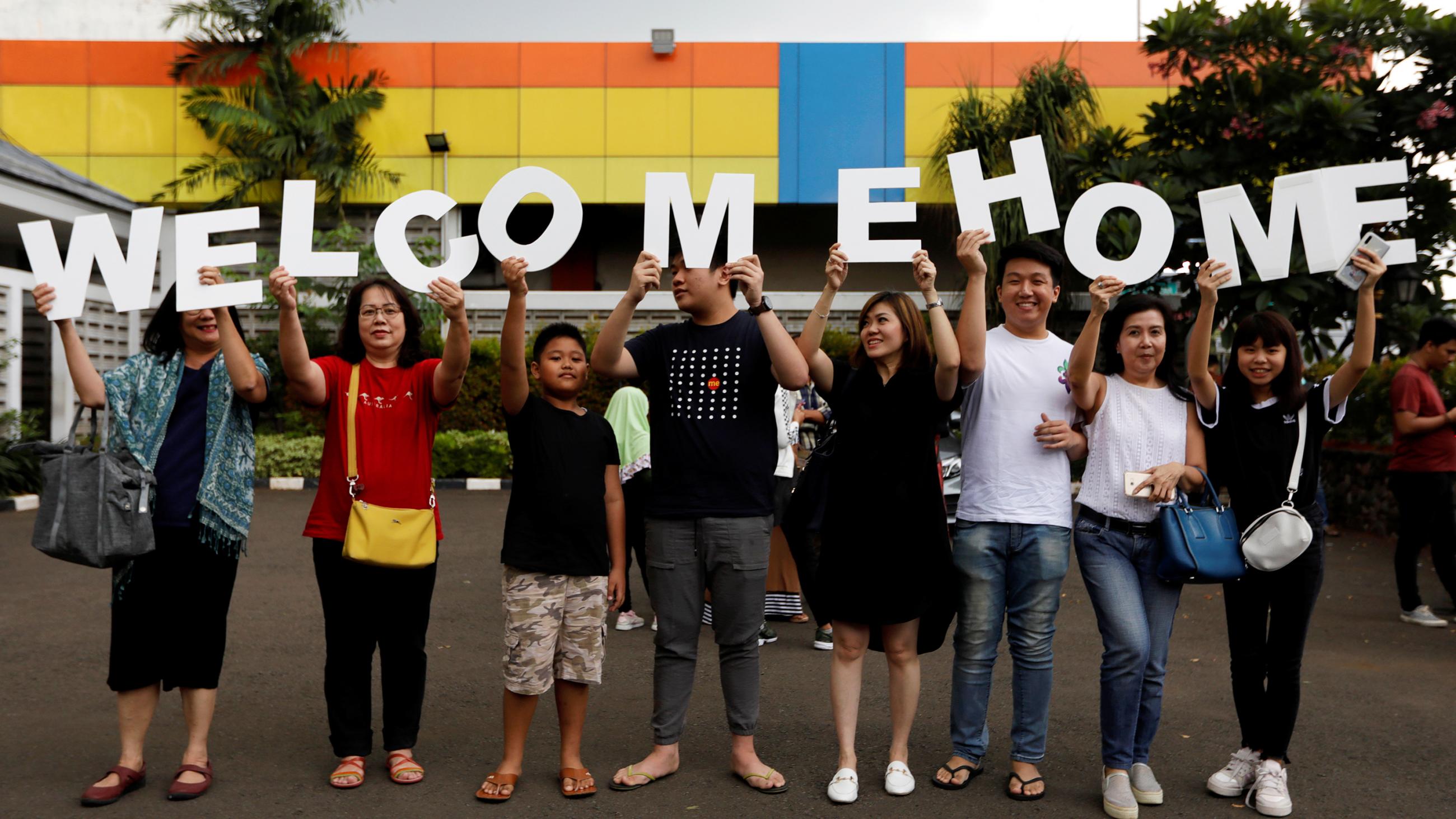  This is a fun photo of a large extended family standing in a parking lot holding a sign that reade welcome home. 
