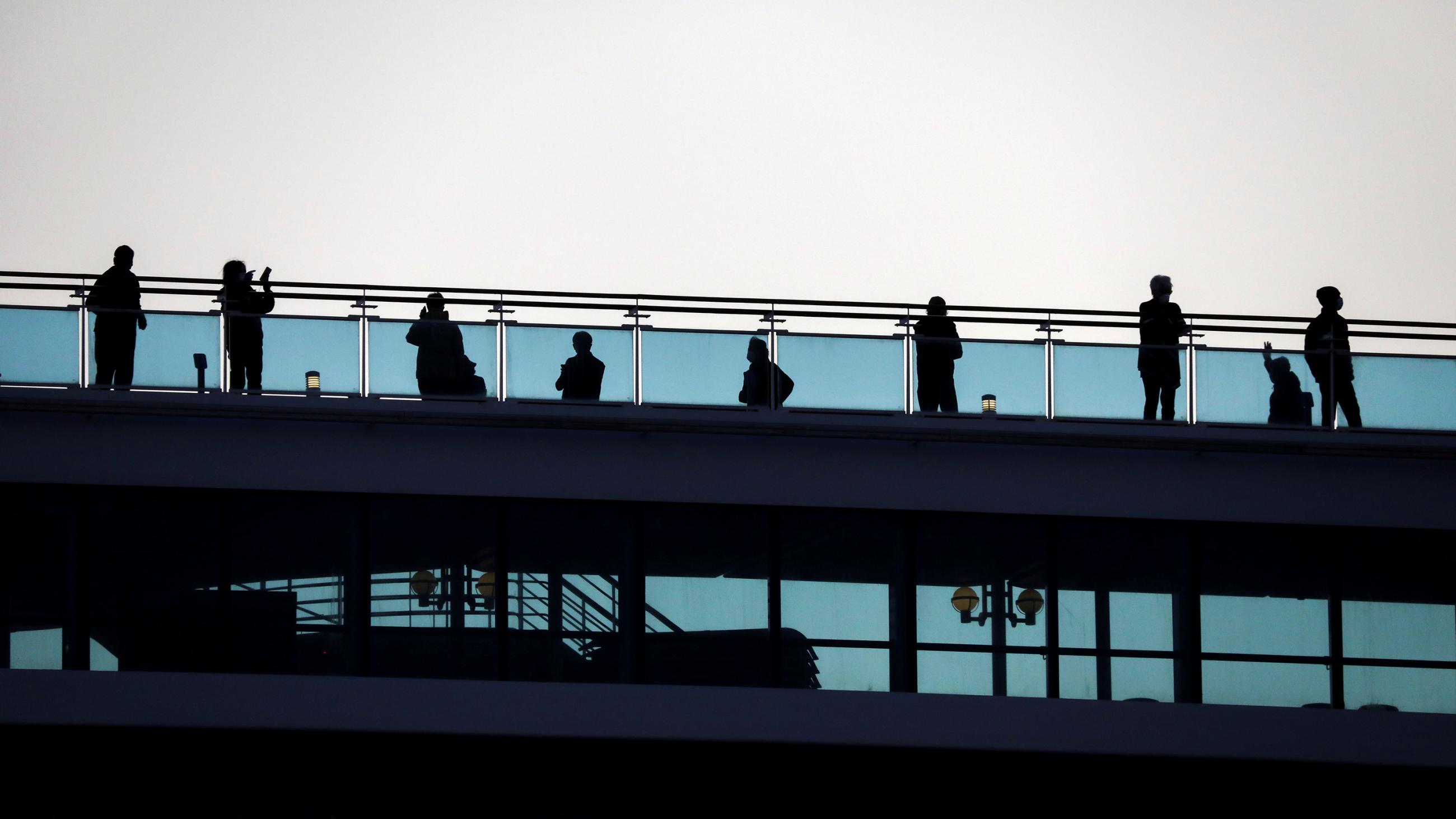 The image shows a couple rows of passengers on two decks, one below the other. They are standing against a bright background and appear as silhouettes. 