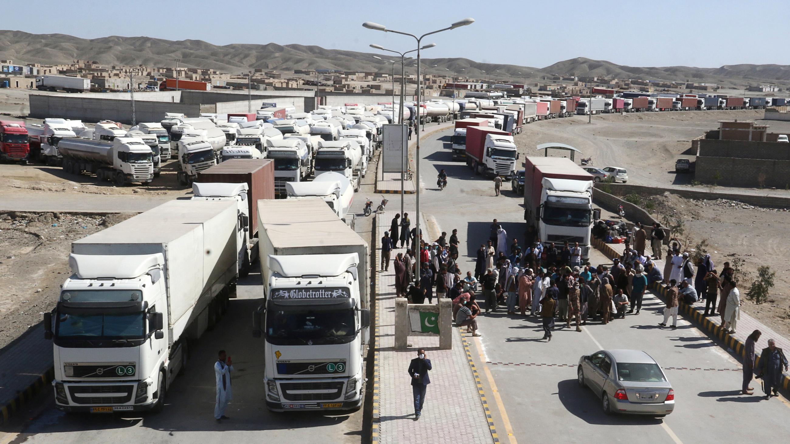 The photo shows the border crossing from a distance of several hundred yards away, showing a huge bottleneck of trucks parked waiting in a sparse landscape. 