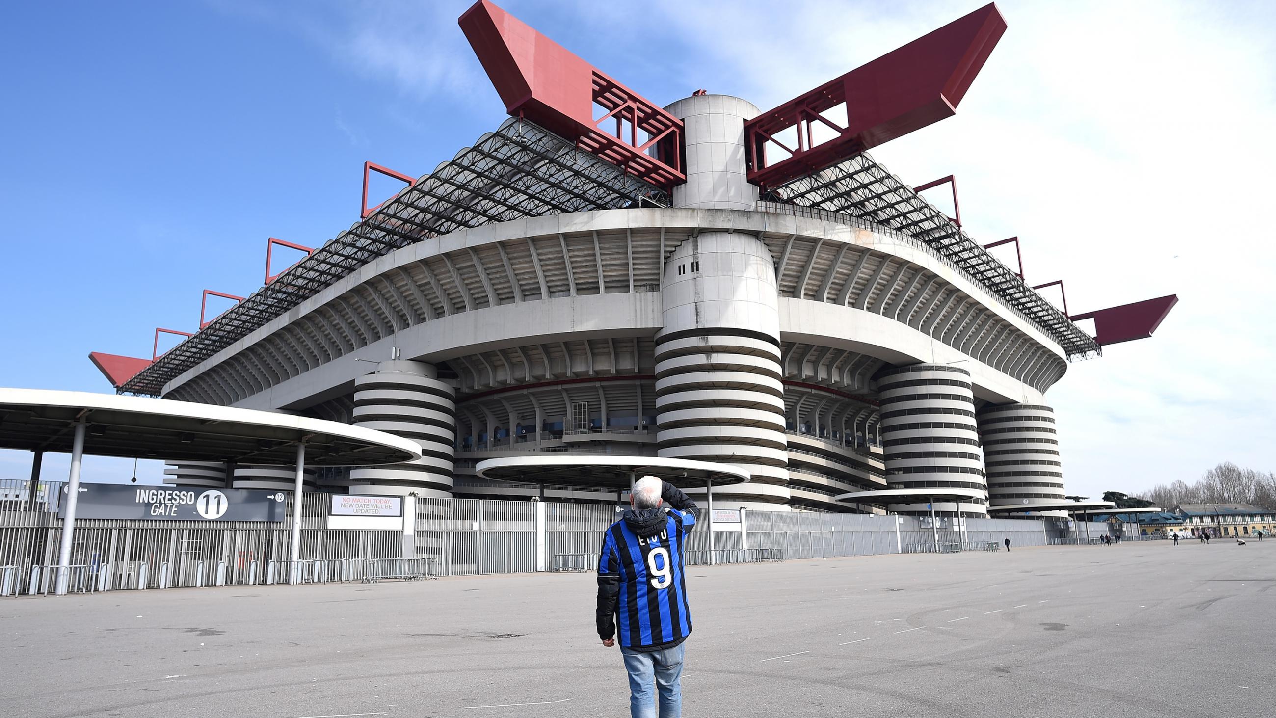 The picture shows a man wearing a fan jersey in an empty lot in front of a massive stadium. 