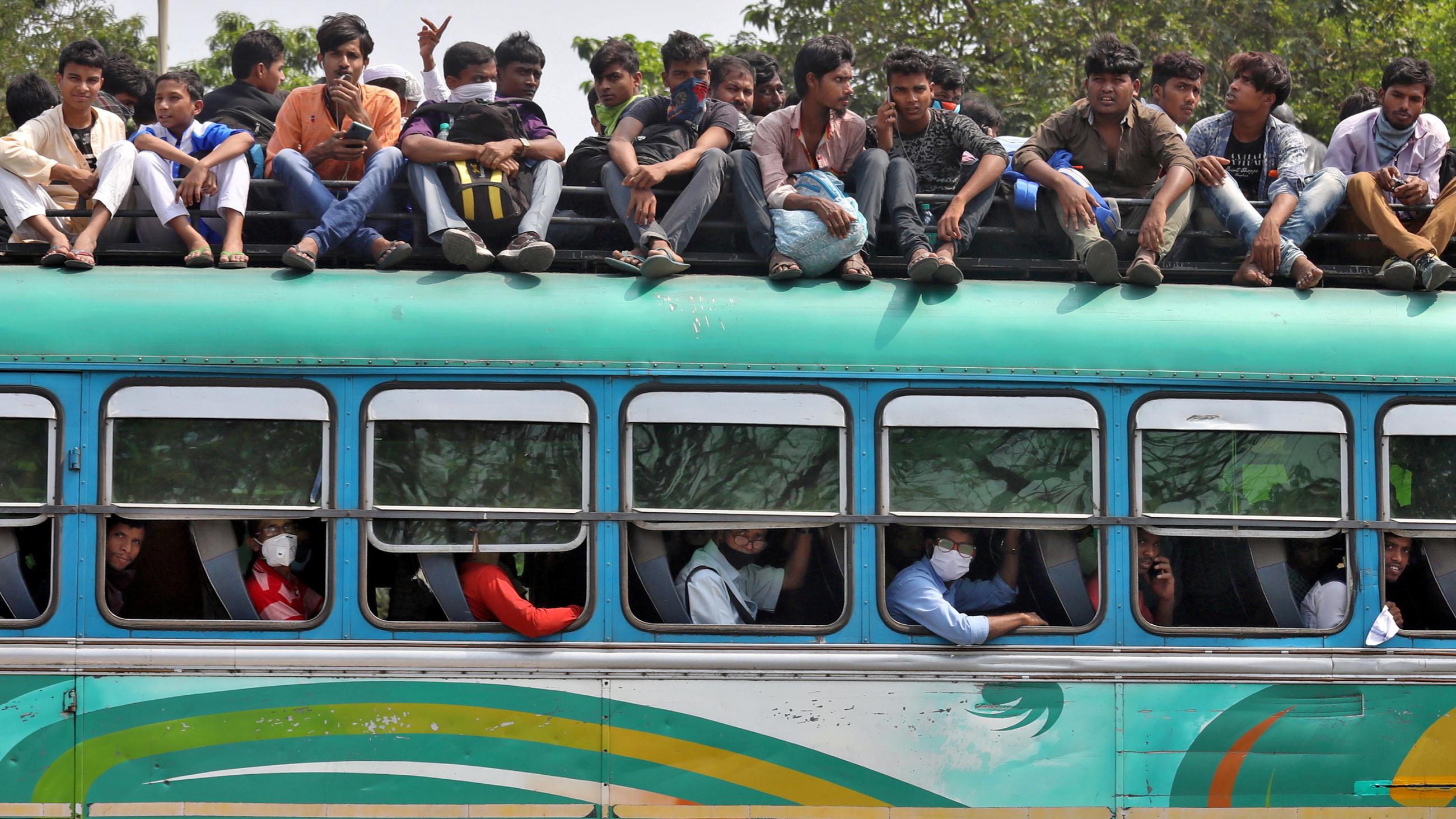 The image shows a green bus, its seats full, with many people sitting on top of the vehicle. 