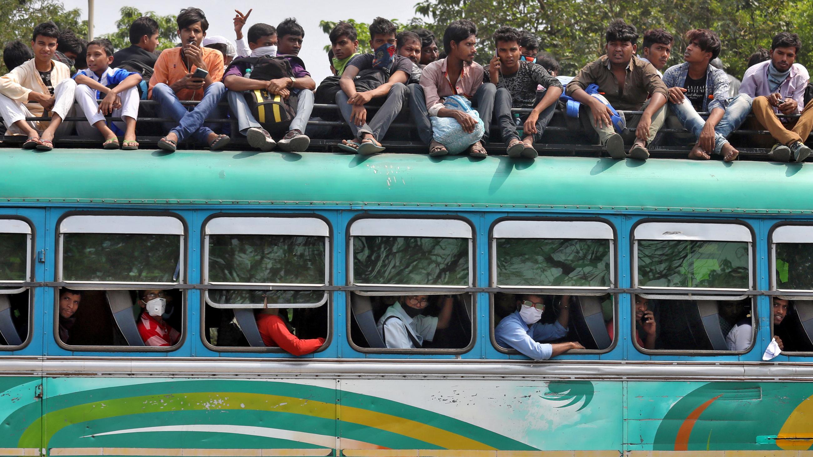 The image shows a green bus, its seats full, with many people sitting on top of the vehicle.