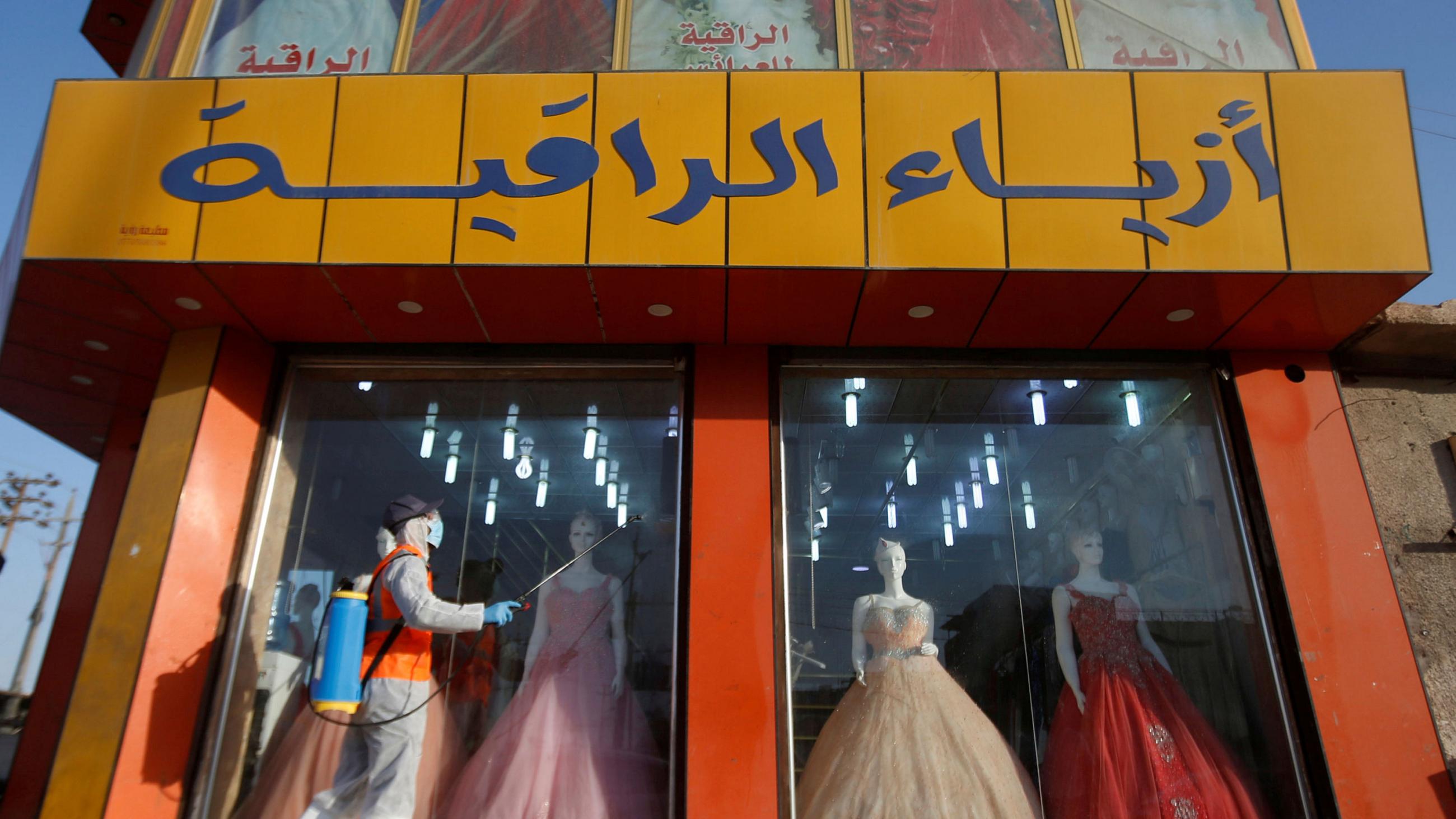 This is an interesting photo showing a colorful dress shop with a worker walking by outside in protective gear spraying disinfectant. 