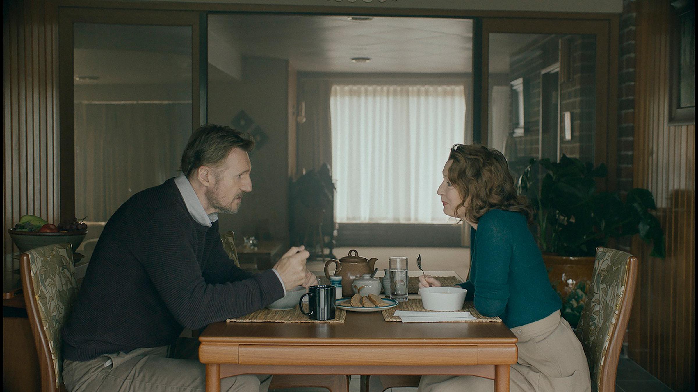 Picture is a production still from the film showing the couple sitting across from each other at their breakfast table. 