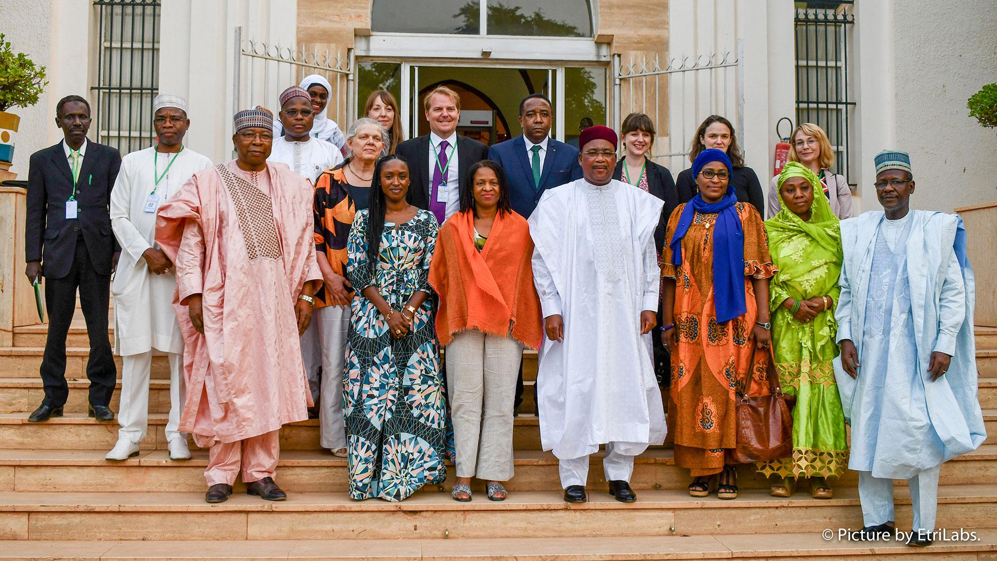 The image shows a dozen or so well dressed officials standing on the steps of a building and posing for the camera. 