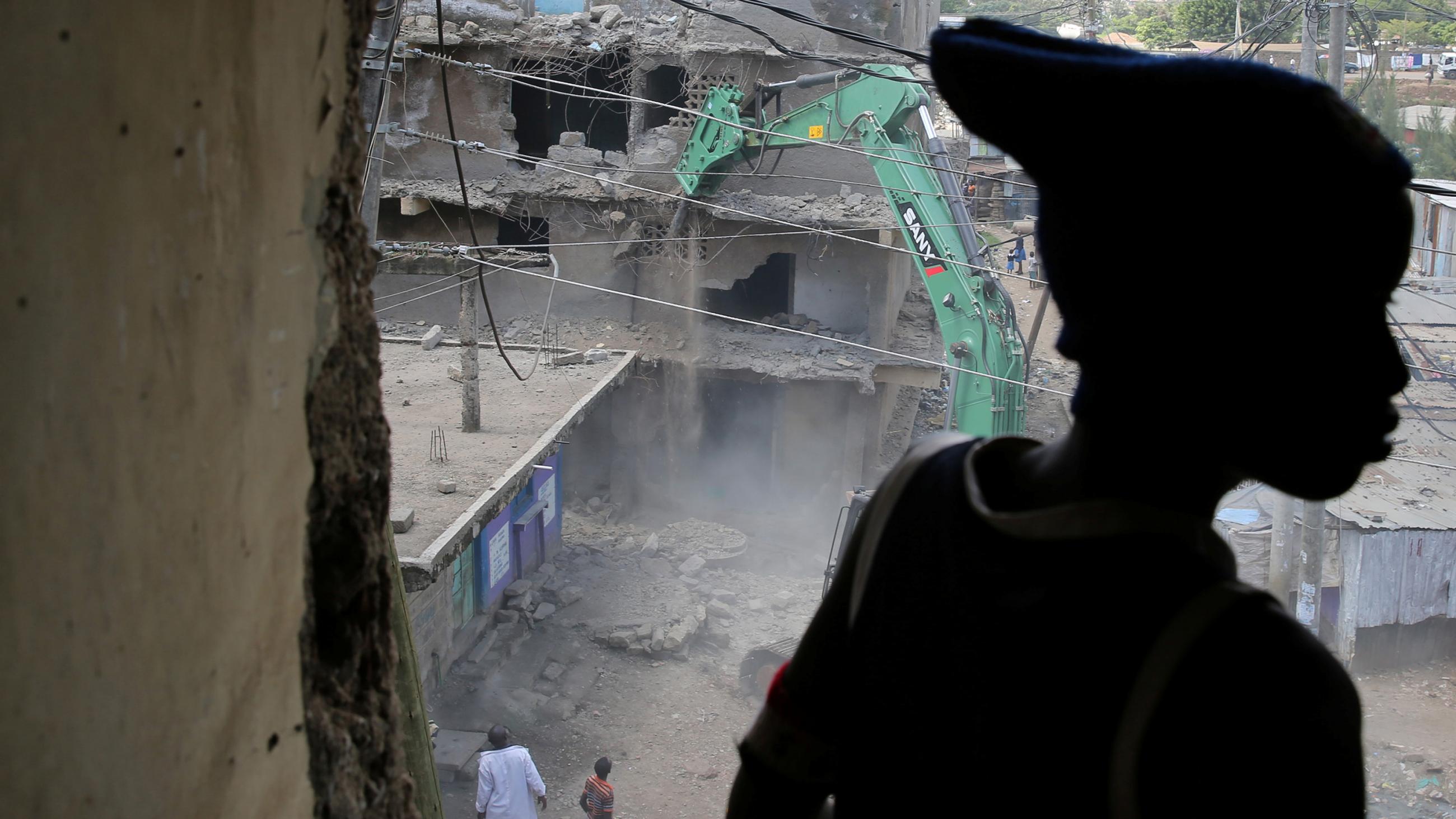 Image shows a building being torn down while the boy watches. He is silhouetted in the foreground. 
