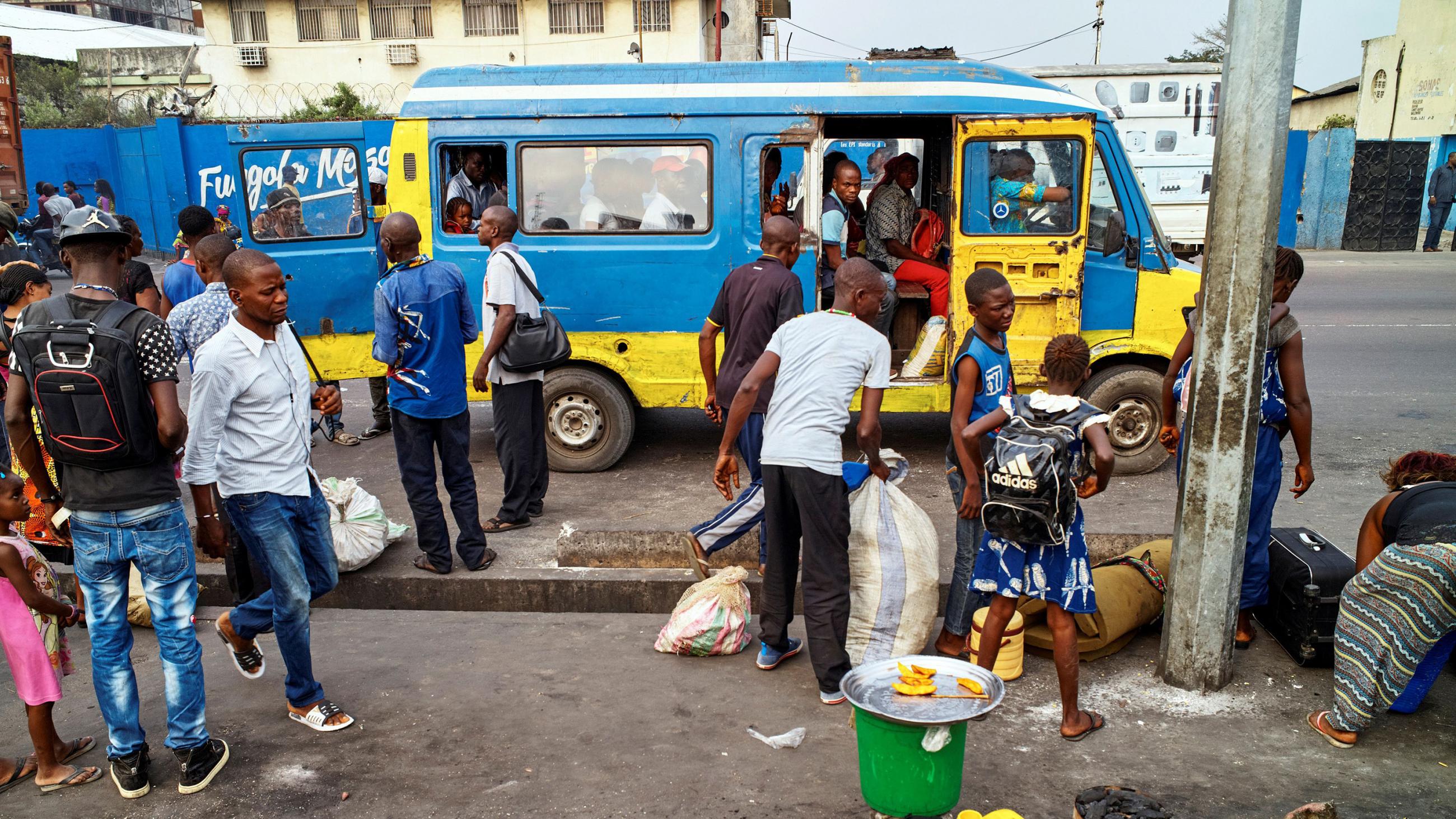 The photo shows a bustling street scene with several people boarding a blue bus. 
