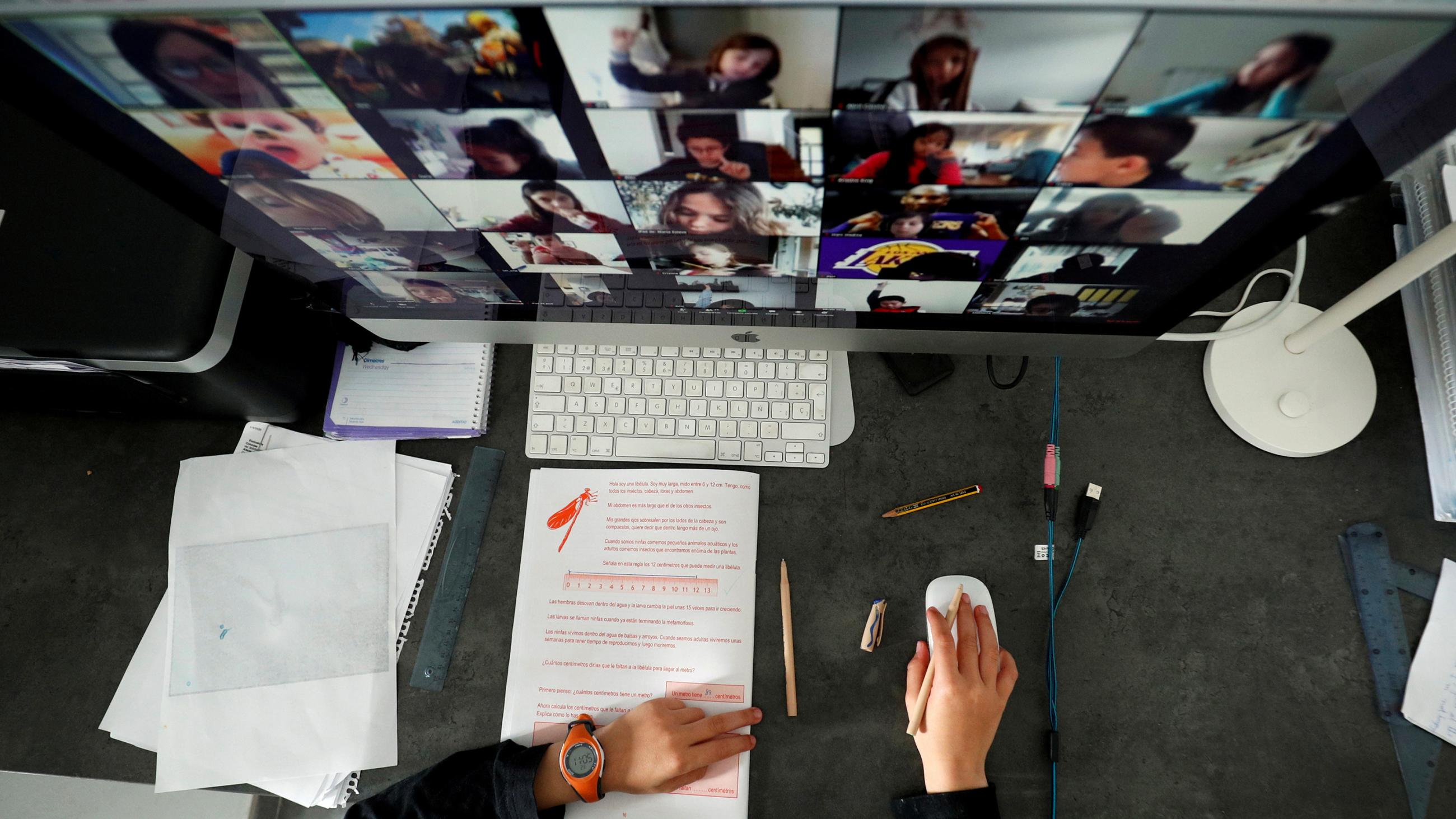  The photo shows a large screen seen from above with the faces of lots of students at remote locations. 