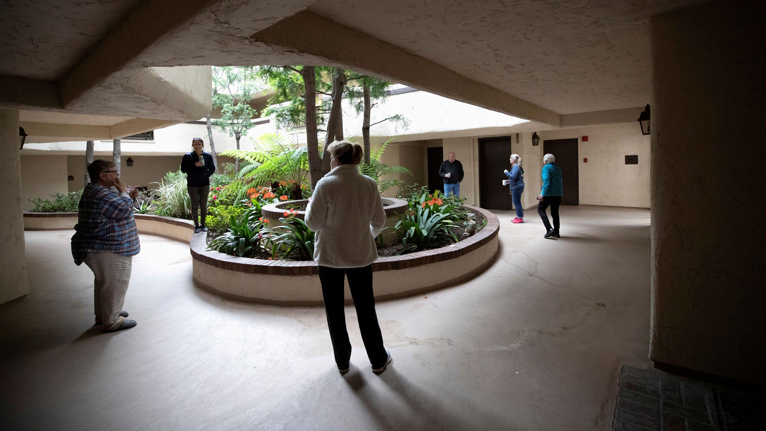 The picture shows half a dozen people in a courtyard standing far apart and talking. 