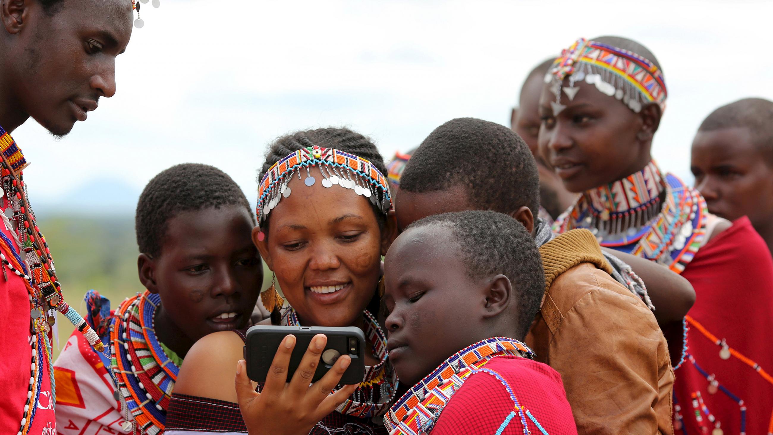 The images shows several girls crowded around a device while a young man looks on. 