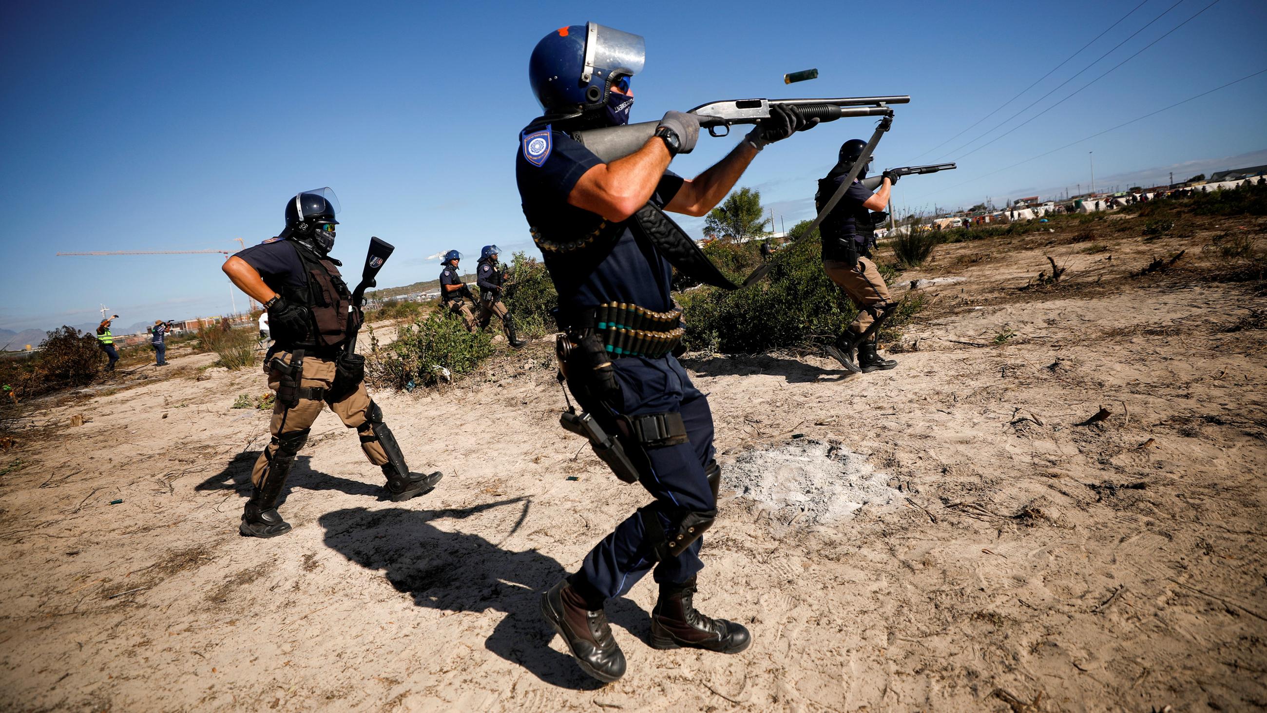 The photo shows police in full riot gear with weapons raised to fire. 