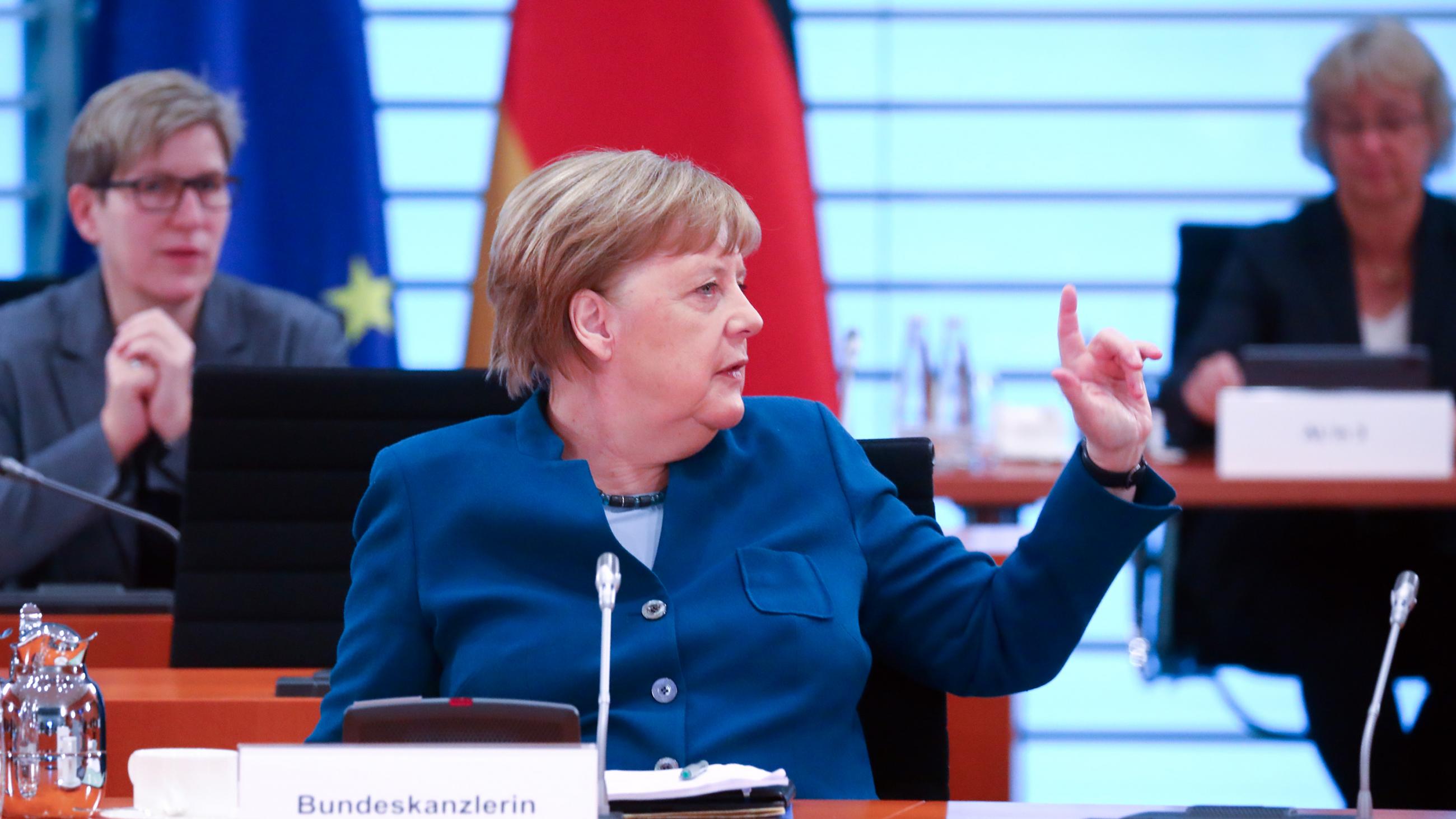 The photo shows the German chancellor at a table turning to her side gesturing to someone off camera. 