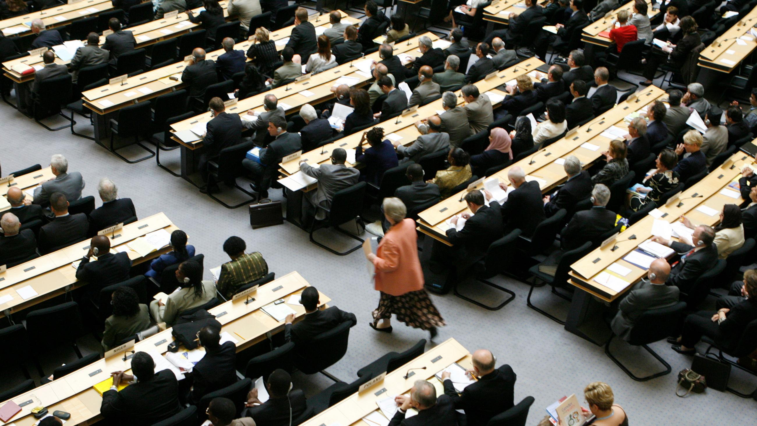 The photo shows a delegate walking up the aisle of a crowded assembly hall. 