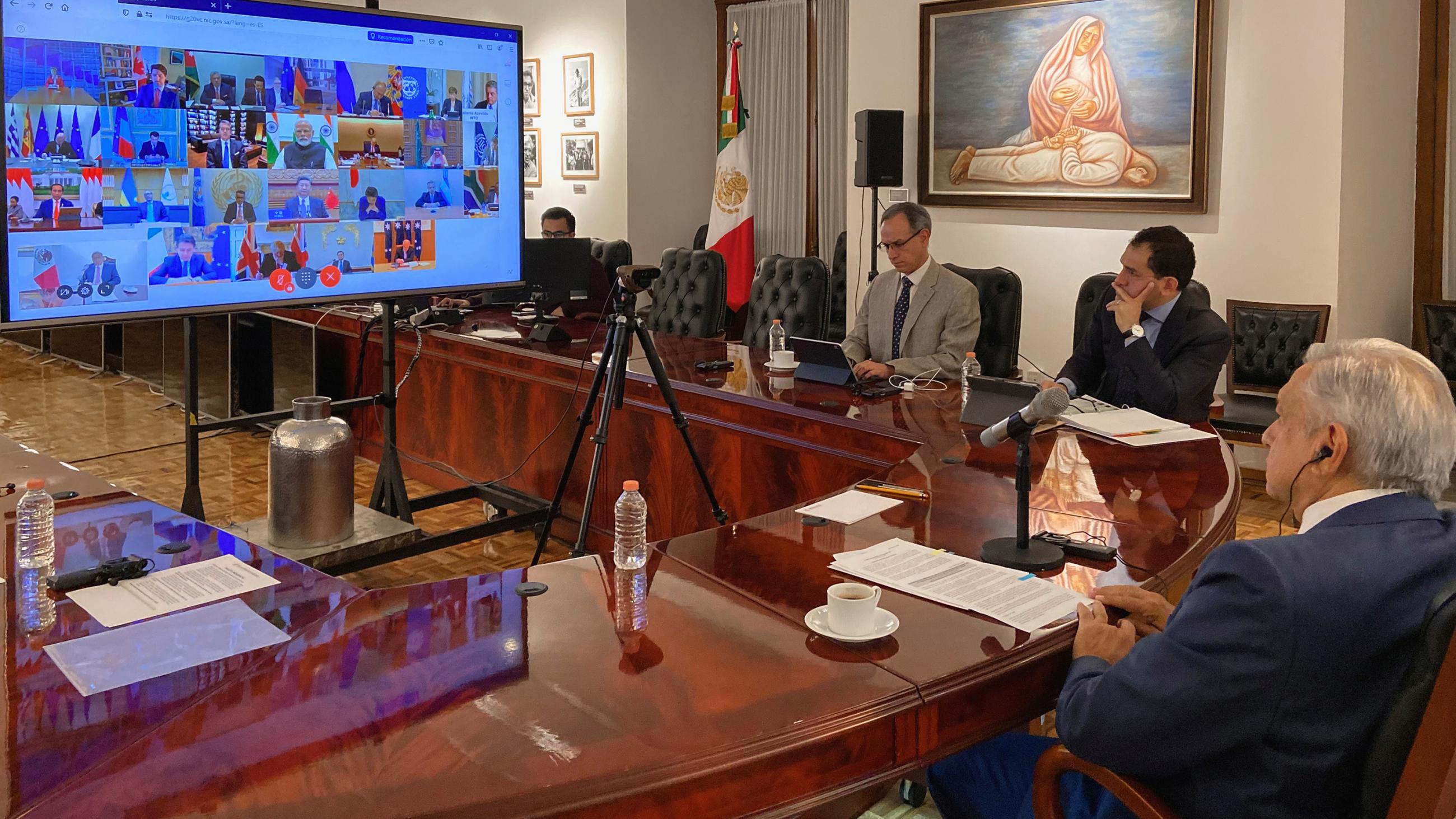 The photo shows the president in a room with a large monitor and several other people sitting nearby. 