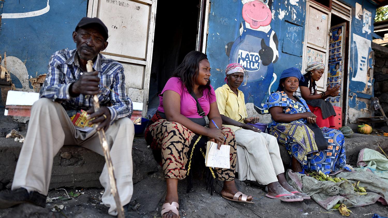 The photo shows a number of women and one man sitting in front of a storefront painted blue and adorned by a large cartoon figure of a cow giving a thumb's up.