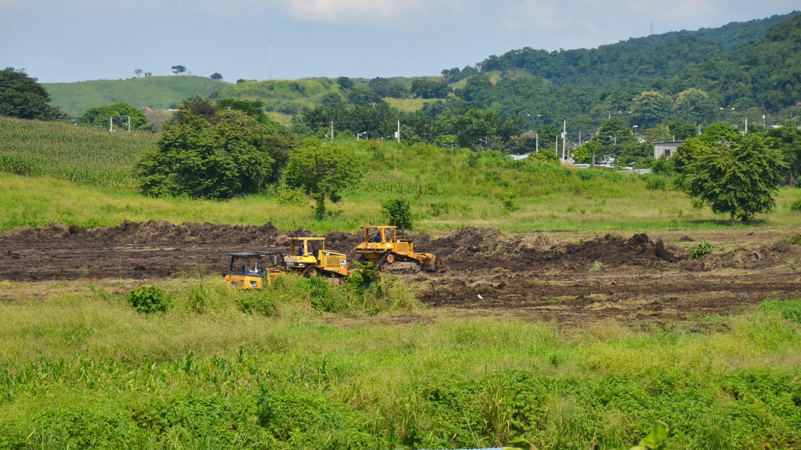 Picture shows a lush green landscape with some heavy machines clearing the ground. 
