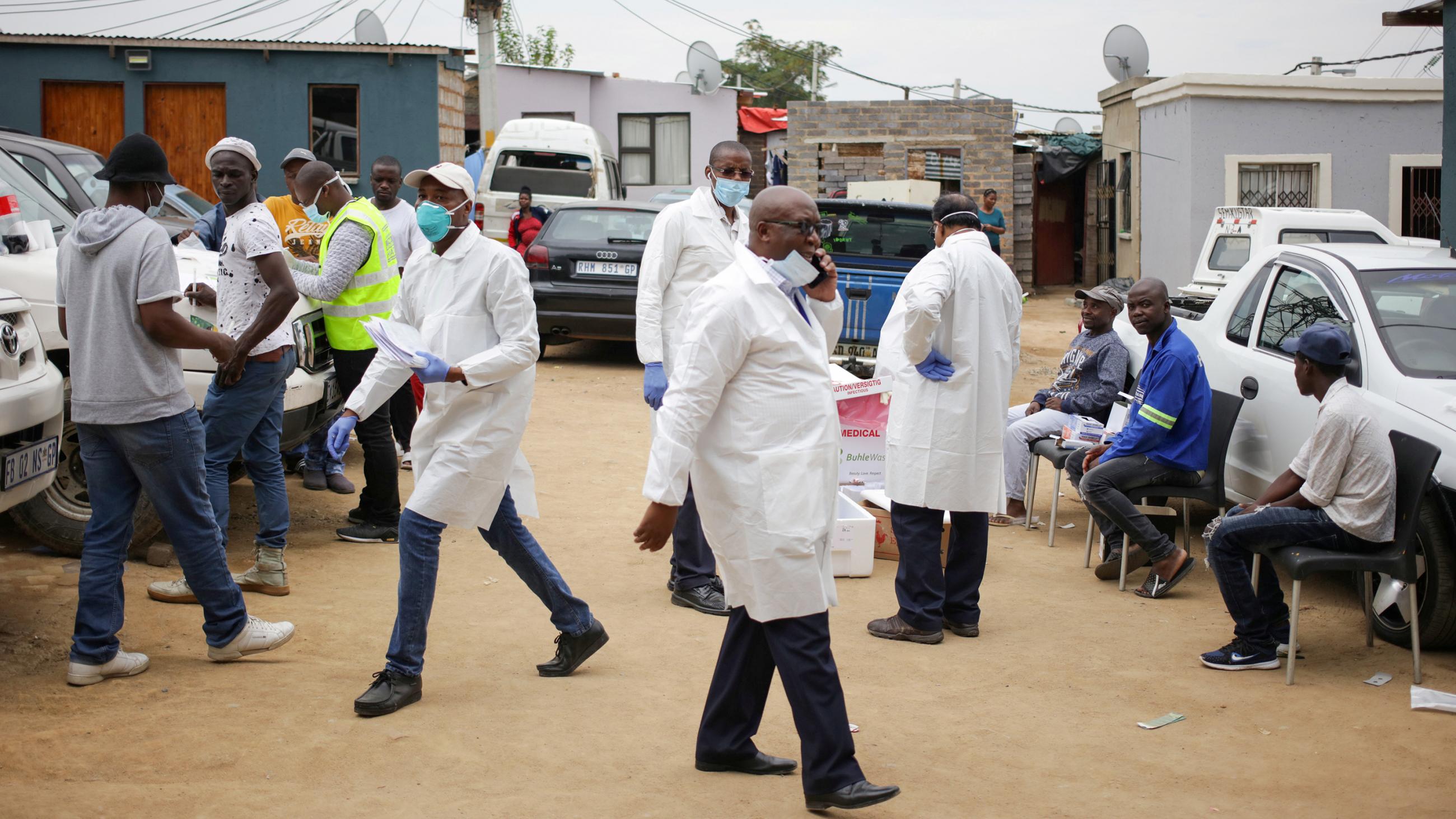 The photo shows about a half dozen health workers wearing white lab coats and a number of civilians waiting to be tested. 