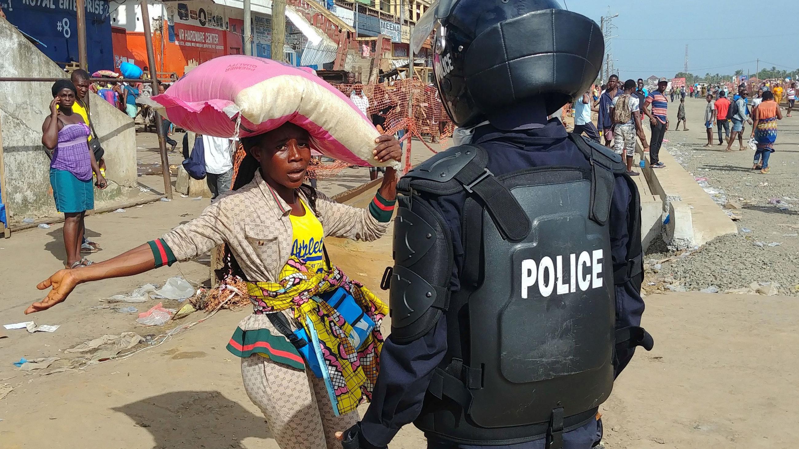 Picture shows a woman with a large sack hoisted above her shoulders confronted by a uniformed police officer. 